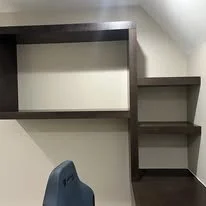 Empty corner with dark brown wall-mounted shelves and a small wooden table in a room with beige walls.