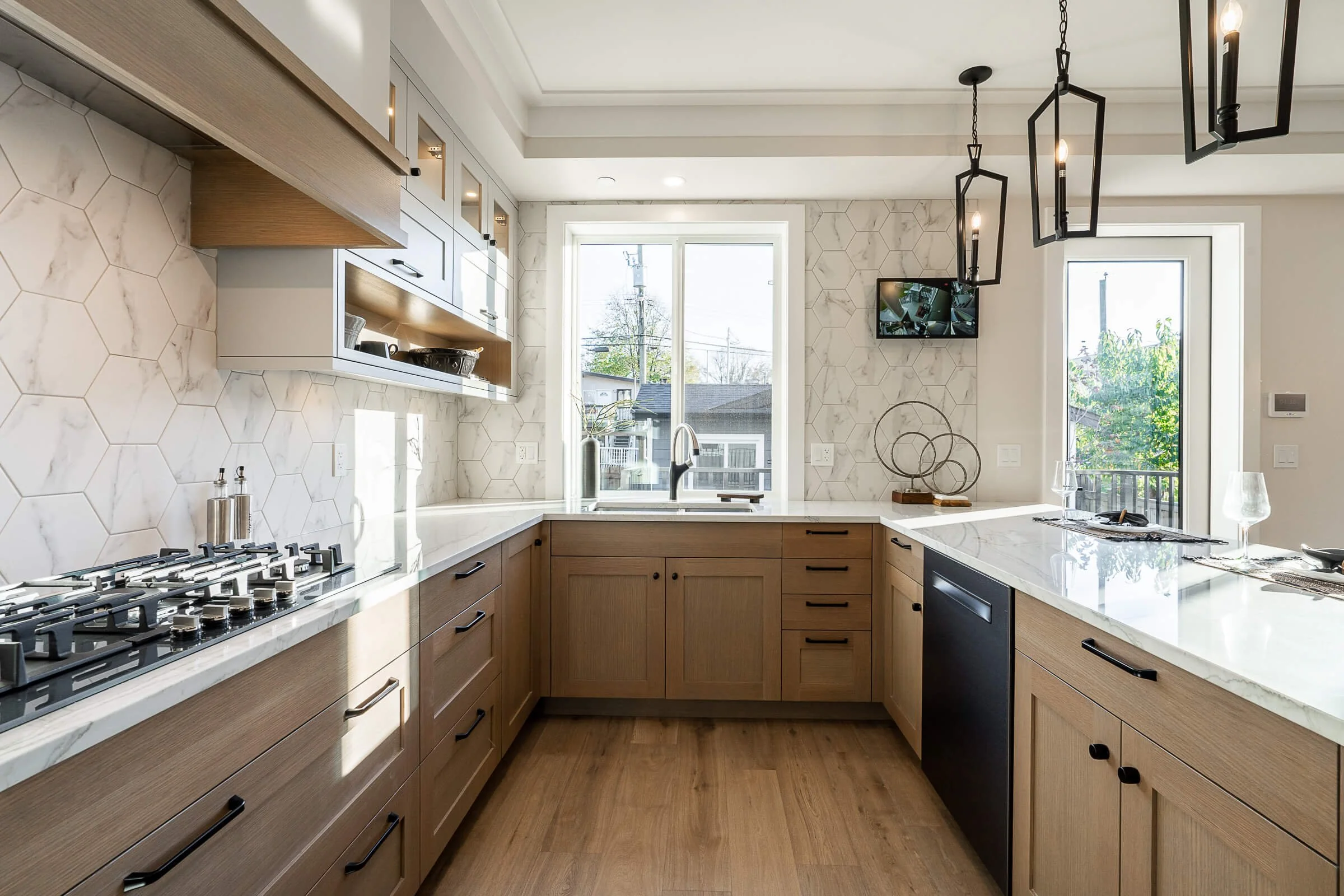 Modern kitchen with wooden cabinets, white marble countertops, honeycomb marble backsplash, black hardware, and pendant lighting fixtures.