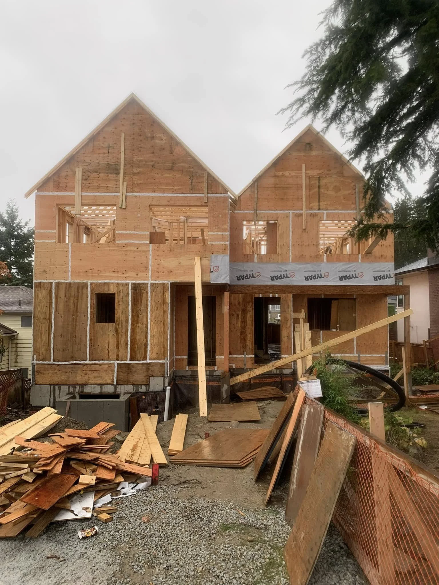 Under construction wooden house framing with construction materials and equipment on the ground.