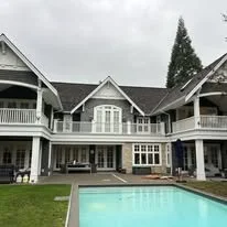 Large white house with multiple stories, balconies, and a swimming pool in the front yard