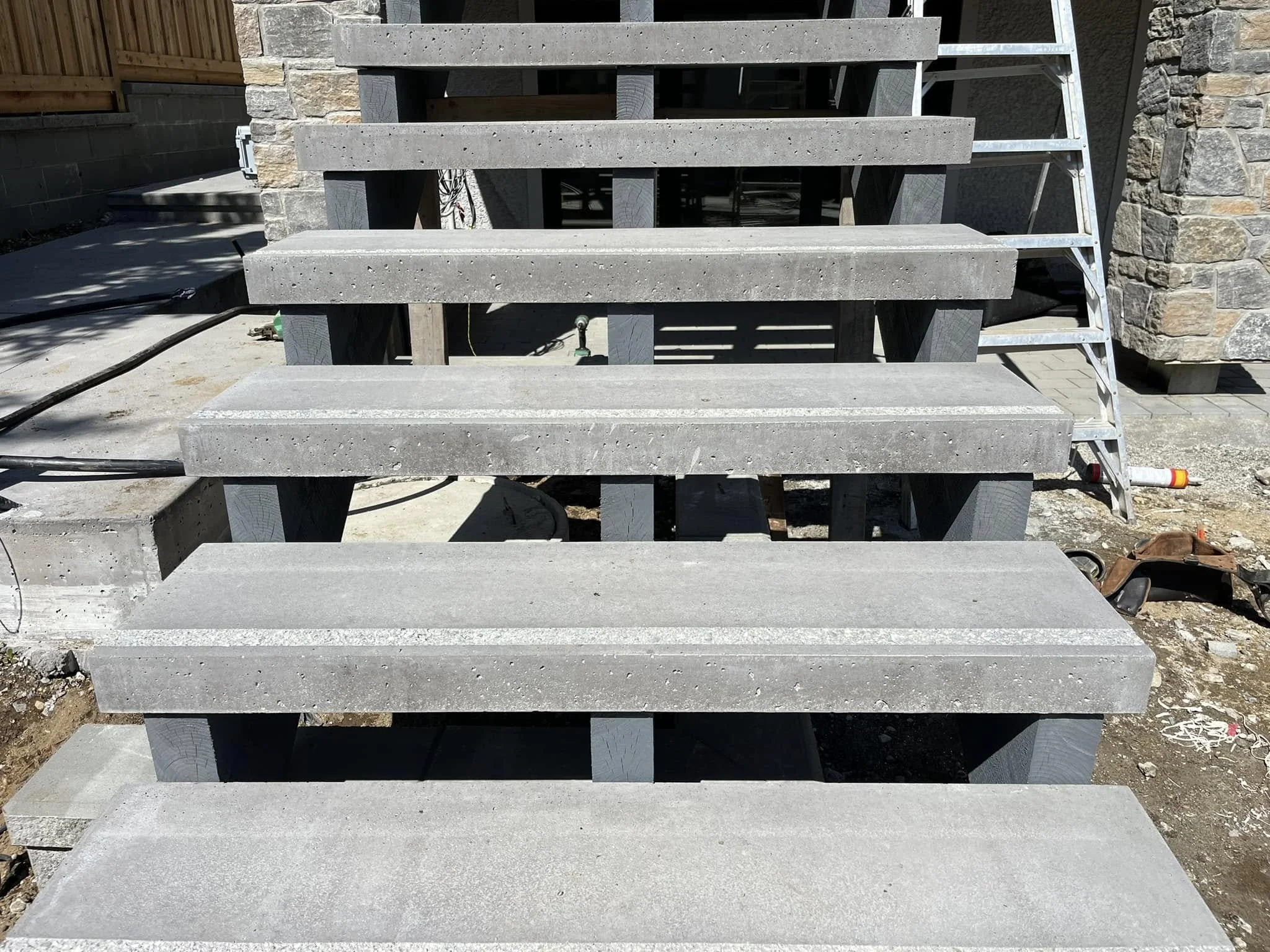 Concrete stairs under construction at a building site, with a ladder on the right side and construction tools and materials around.