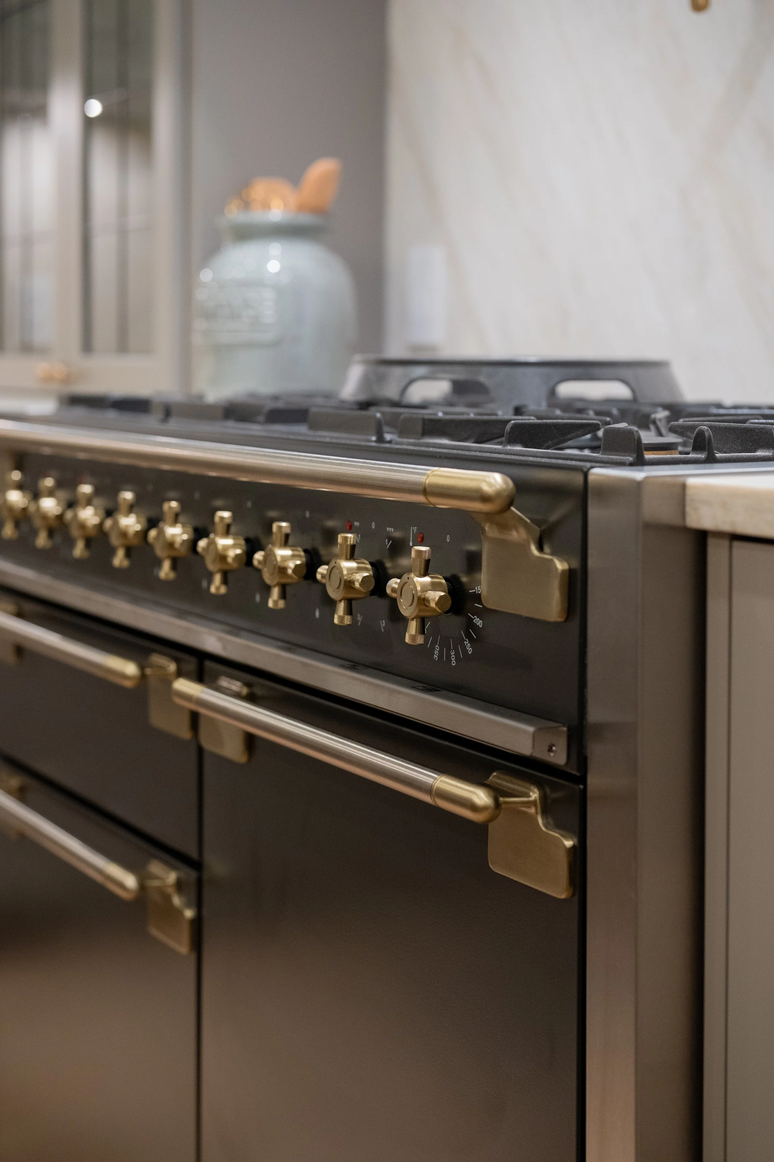 Close-up photograph of a modern black and gold gas stove with multiple burners and knobs in a kitchen.