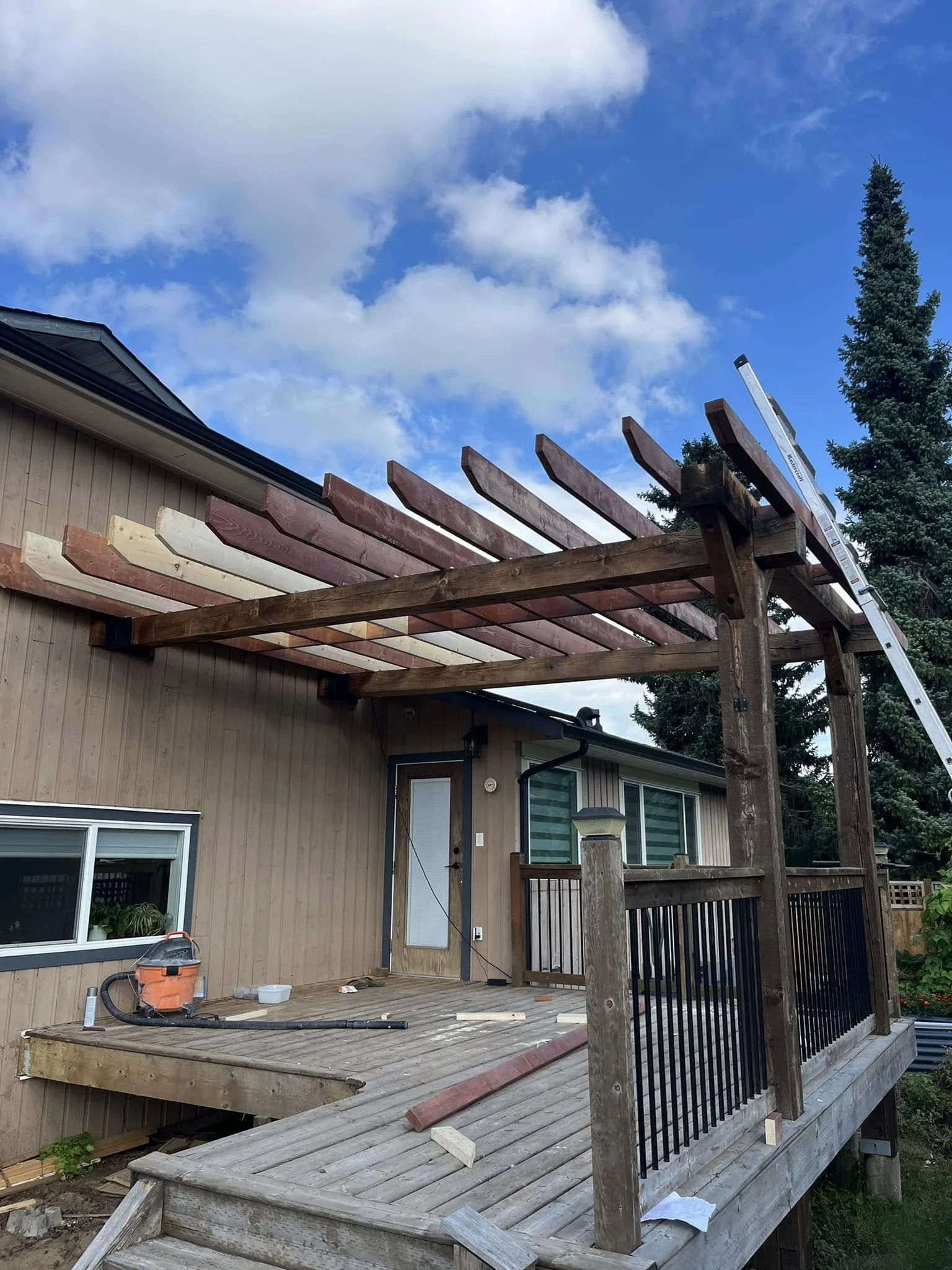 Construction of a wooden deck and pergola on the back of a house, with building tools and materials present.