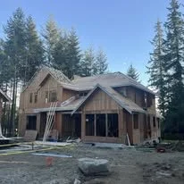Newly constructed house surrounded by trees with unfinished exterior and construction materials nearby.