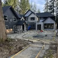 Construction site in front of a modern blue house, with concrete pathways being built and construction materials around.