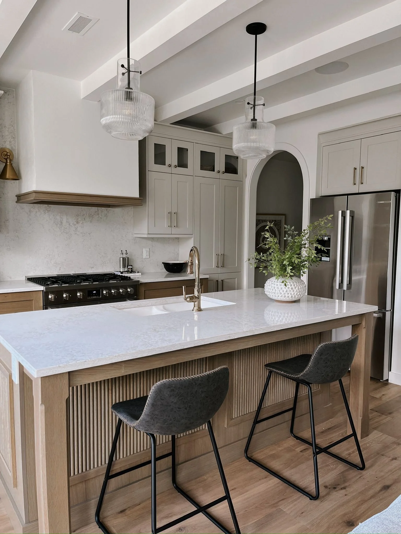 Modern kitchen with white cabinets, a marble island, black chairs, pendant lights, and stainless steel refrigerator.