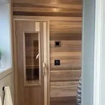 A door with a glass panel next to a wooden wall, with a window and a plant beside it.