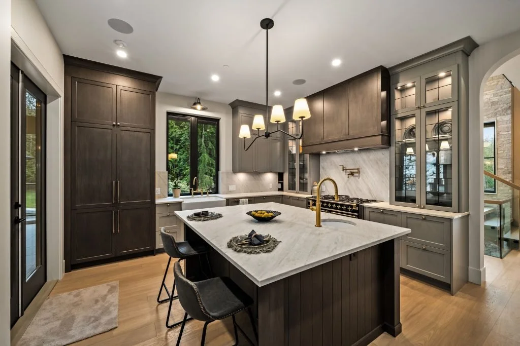 Modern kitchen with dark and gray cabinets, white marble countertop, gold faucet, and a chandelier with multiple shades.
