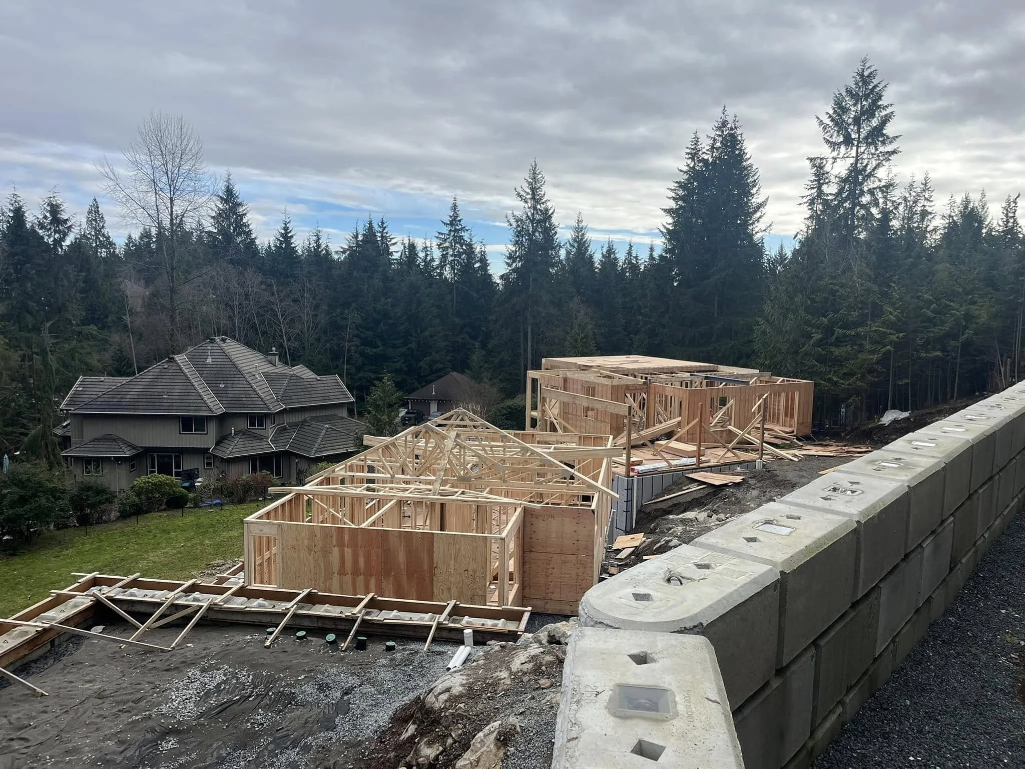 Construction site with wooden framing for new houses, with trees and a cloudy sky in the background.