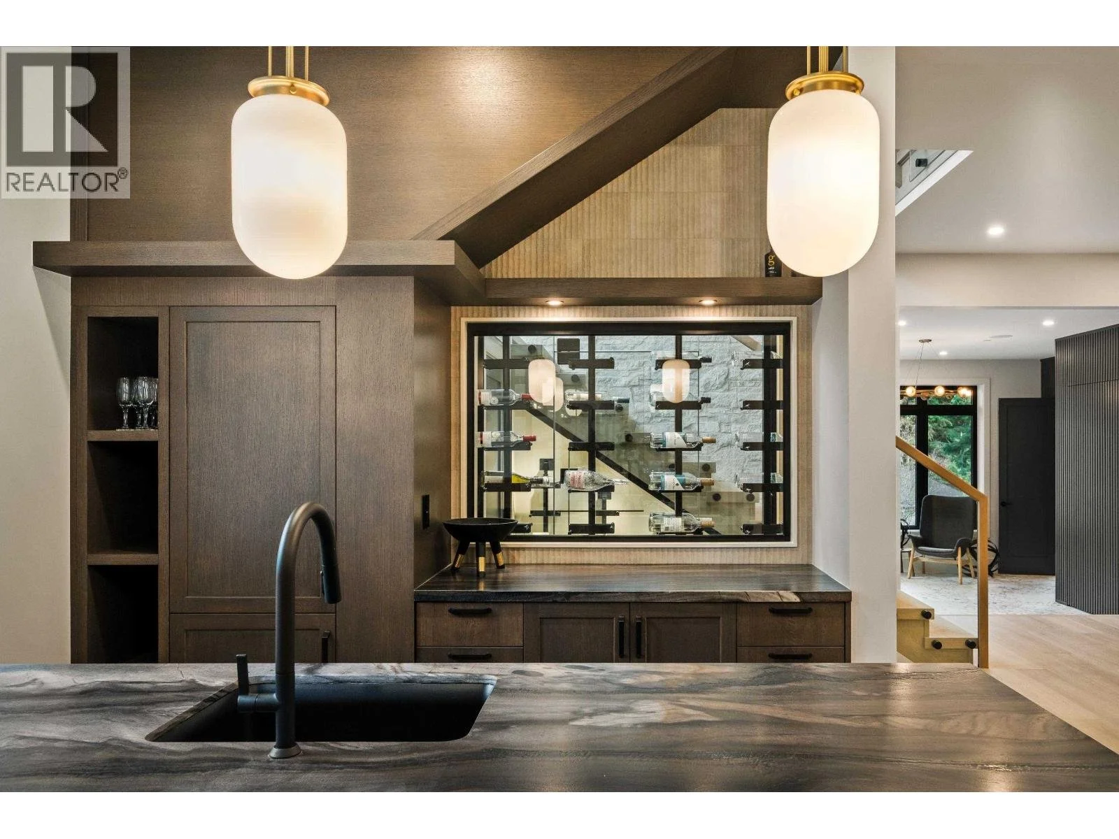 Modern kitchen and living area with pendant lights, wine display, and staircase.