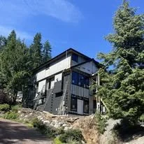 Modern black and white house on a hillside surrounded by trees under a blue sky