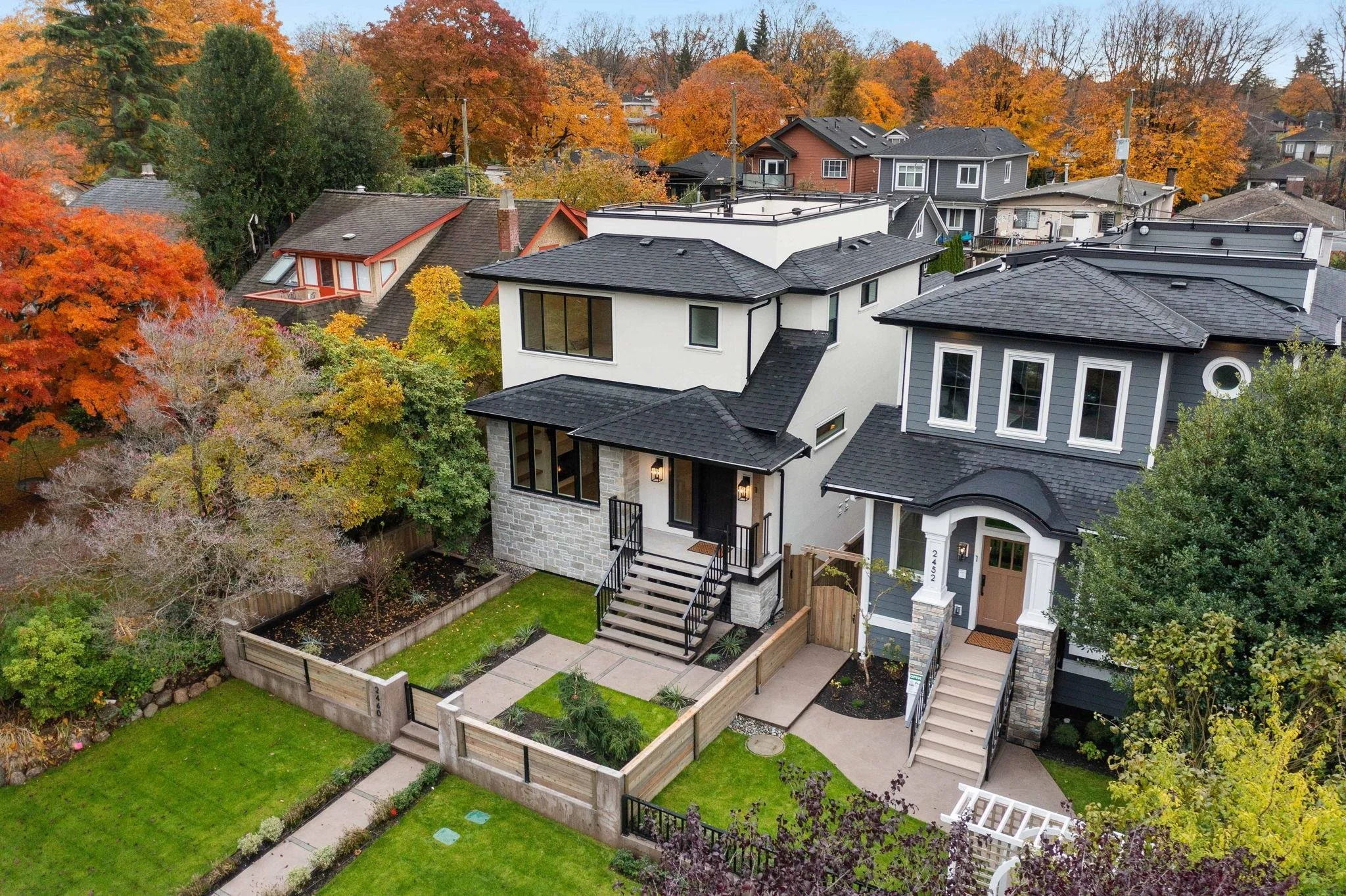 Aerial view of modern houses with landscaped yards, trees with fall foliage, and a neighborhood street.