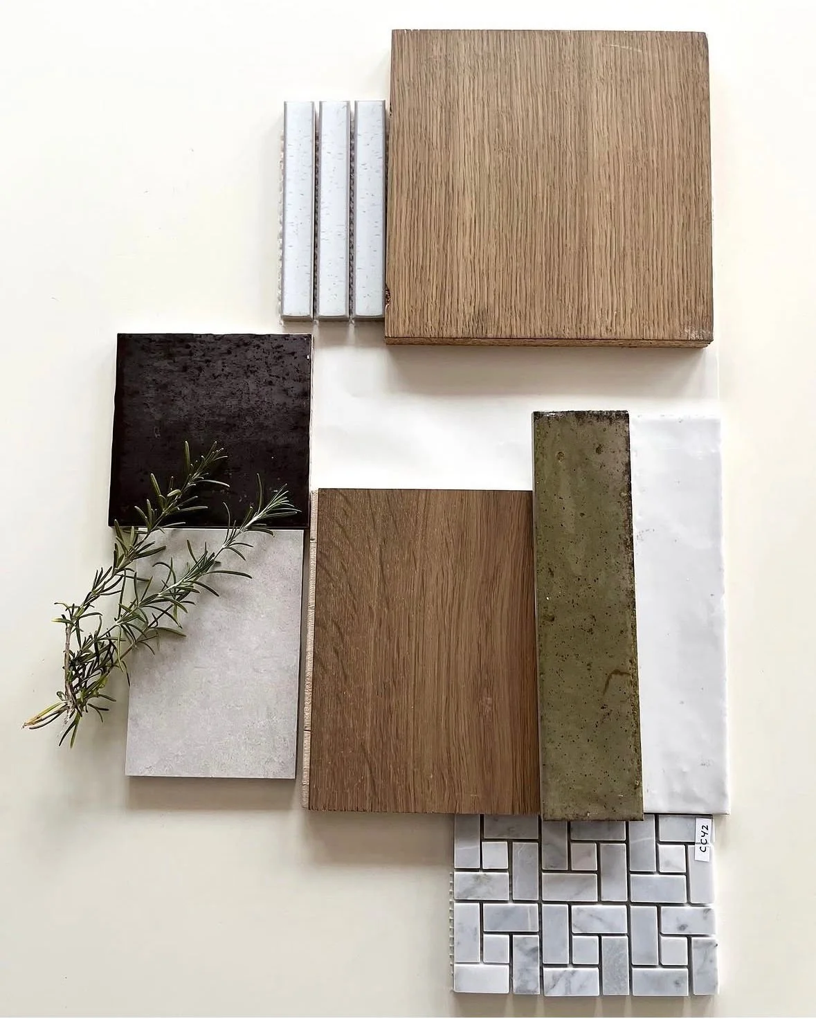 Arrangement of various tile samples including wood, marble, stone, and mosaic with a sprig of greenery for interior design.