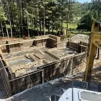 Construction site with a wooden framework for a building, surrounded by trees.