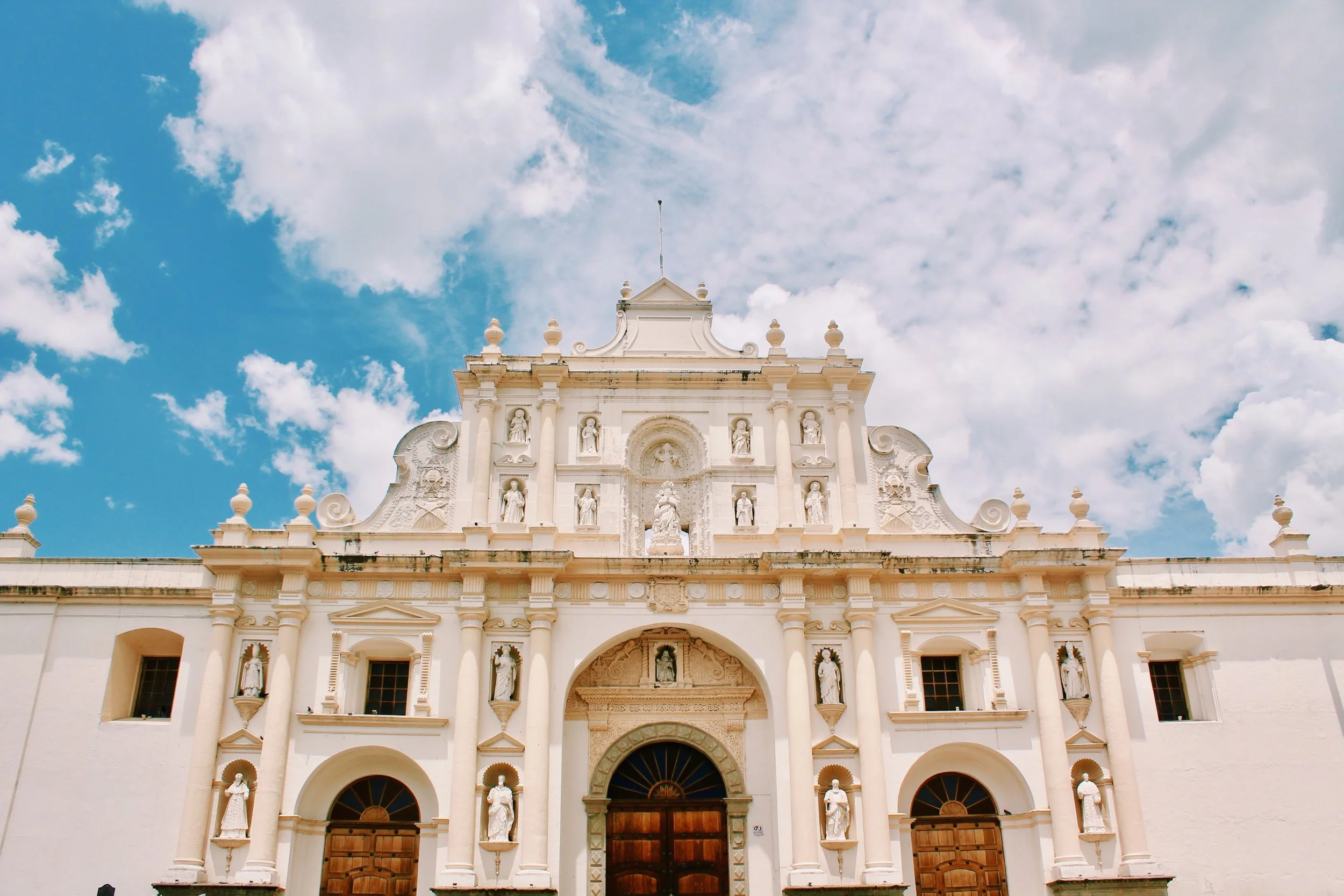 Front view of a white historic church with decorative statues and architecture, under a partly cloudy blue sky.
