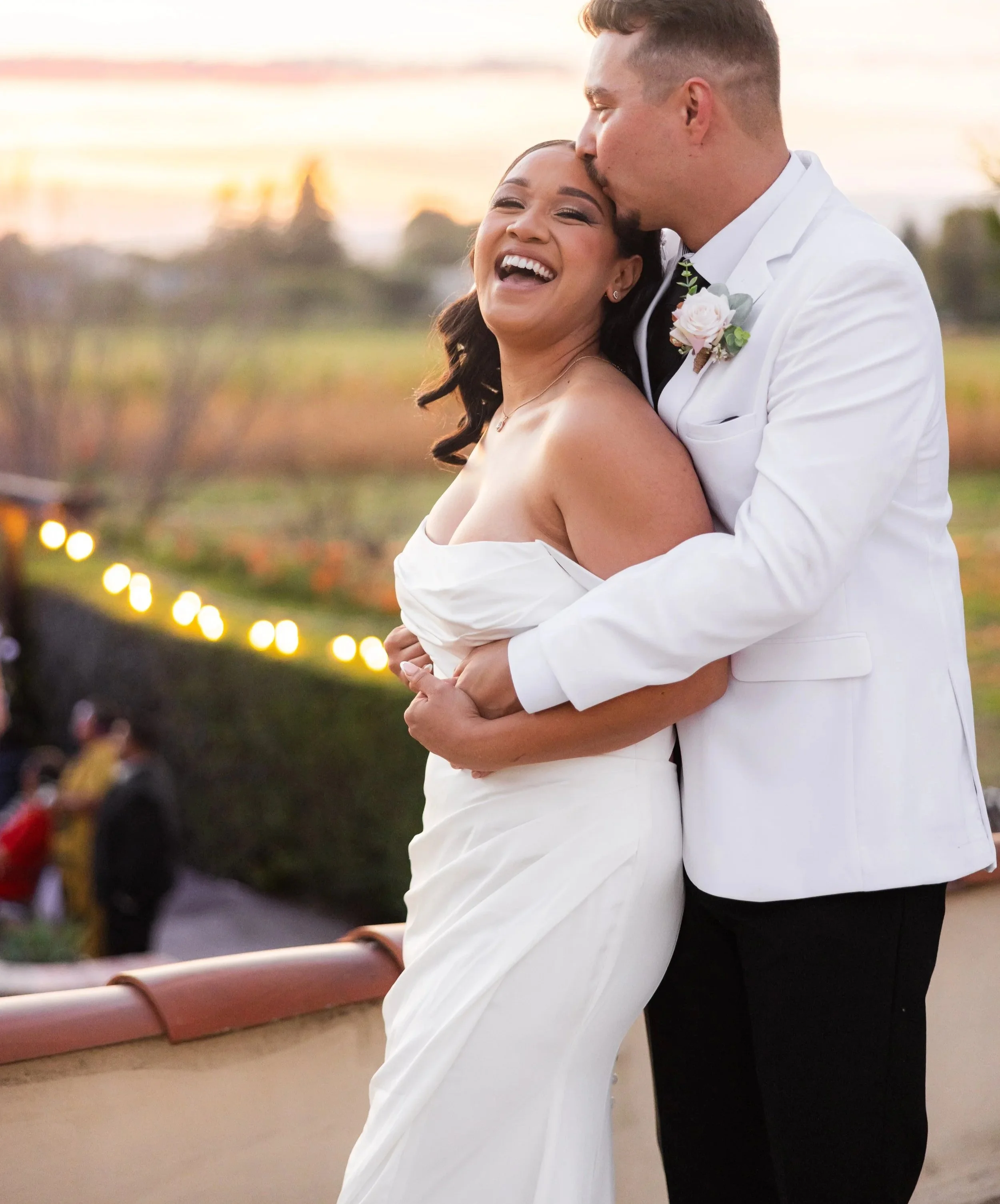 A happy bride and groom sharing a kiss outdoors during sunset at their wedding reception.