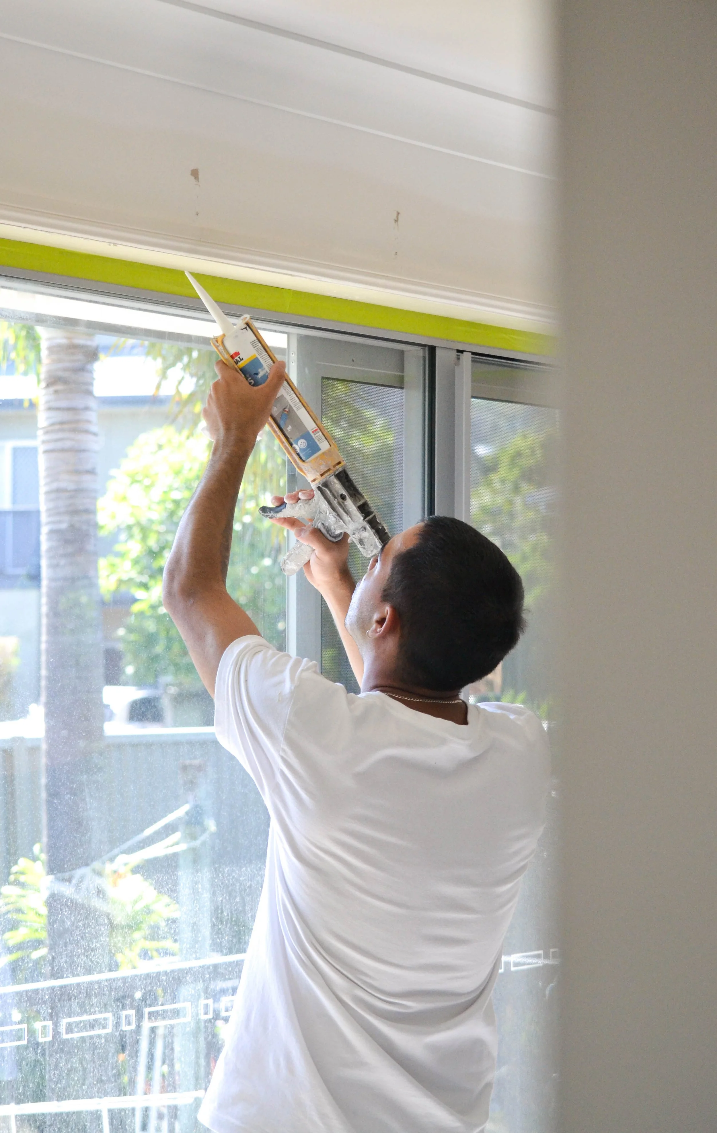 A person using a laptop with an open Google Calendar on the screen, sitting at a table with a black planner or portfolio in the foreground and a green potted plant in the background.