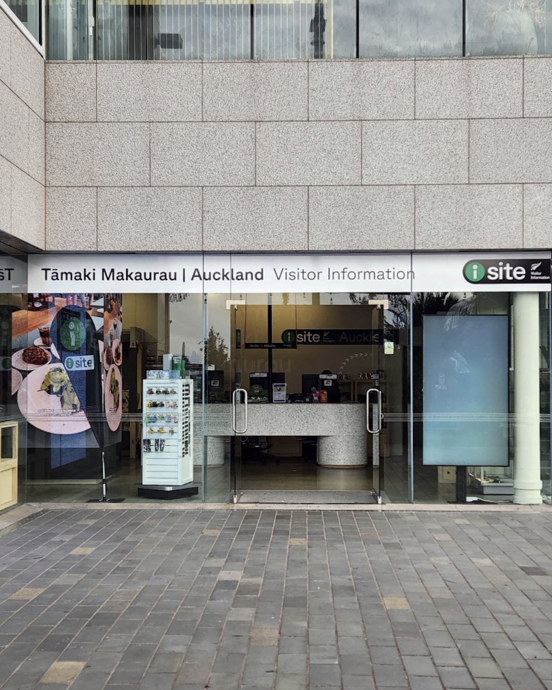 Visitor information kiosk at Tamaki Makaurau (Auckland), New Zealand, with signage and digital displays outside a modern building.