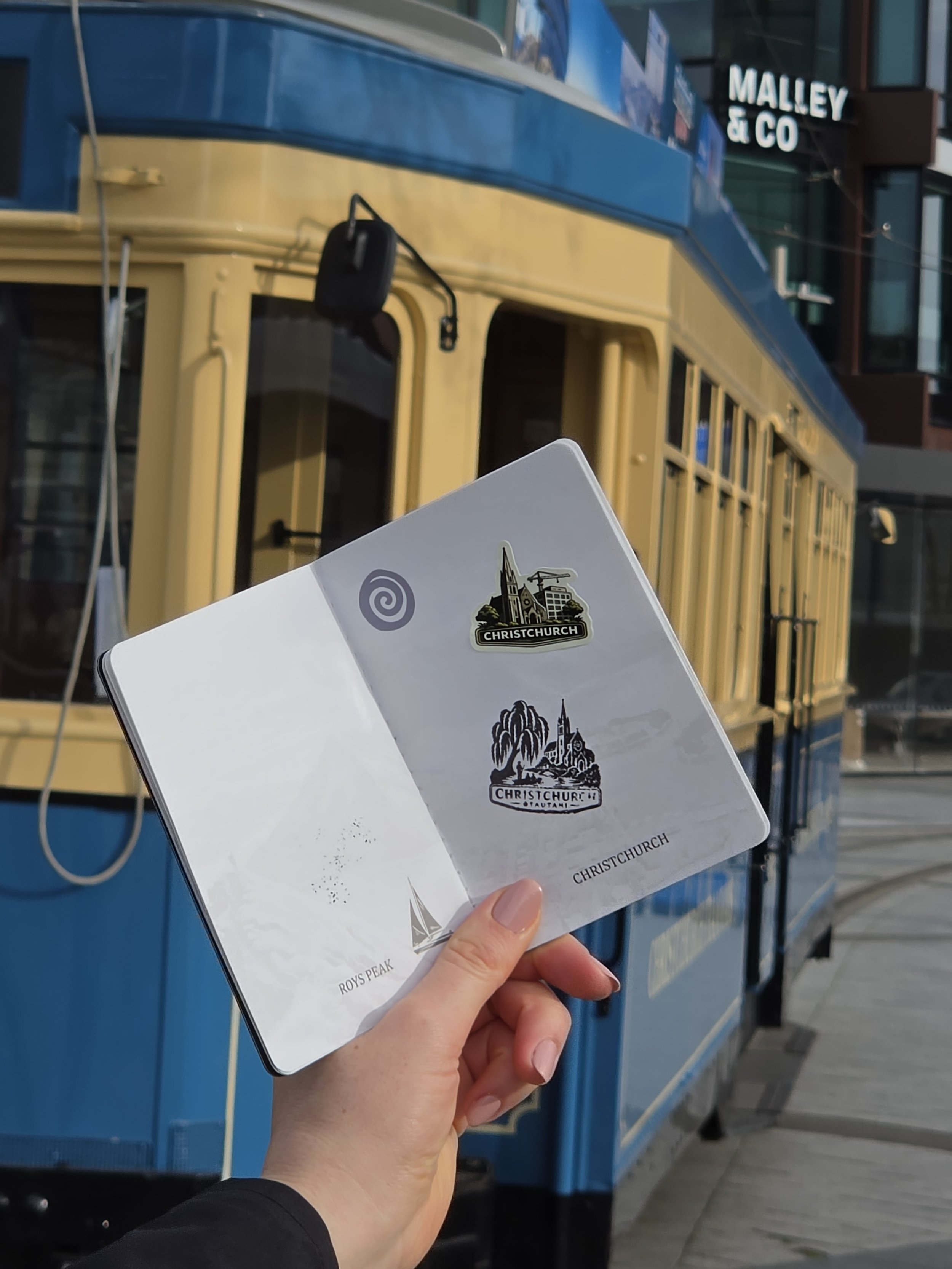 Person holding a pamphlet with Christchurch landmarks in front of a blue tram in Christchurch, New Zealand.