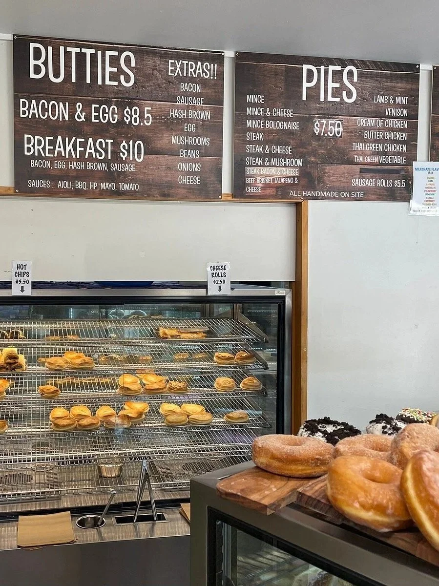 Menu signs featuring options for butties and pies, with prices and available fillings, and a display case of baked goods including donuts and pastries.