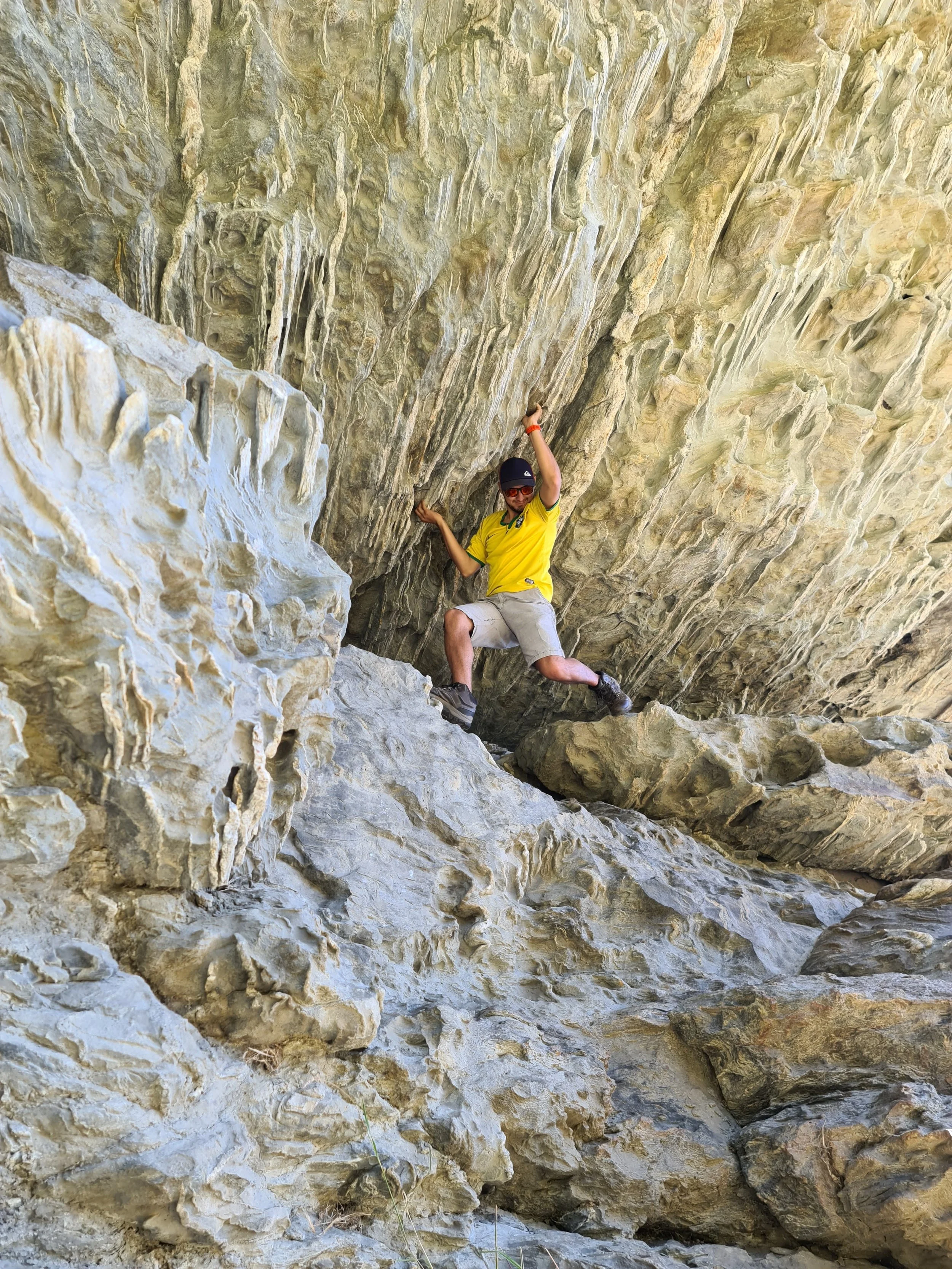 wye creek  A person wearing a yellow shirt, sunglasses, and a cap rock climbing or sitting on a large rock formation inside a cave with a textured, rocky, ceiling overhead.