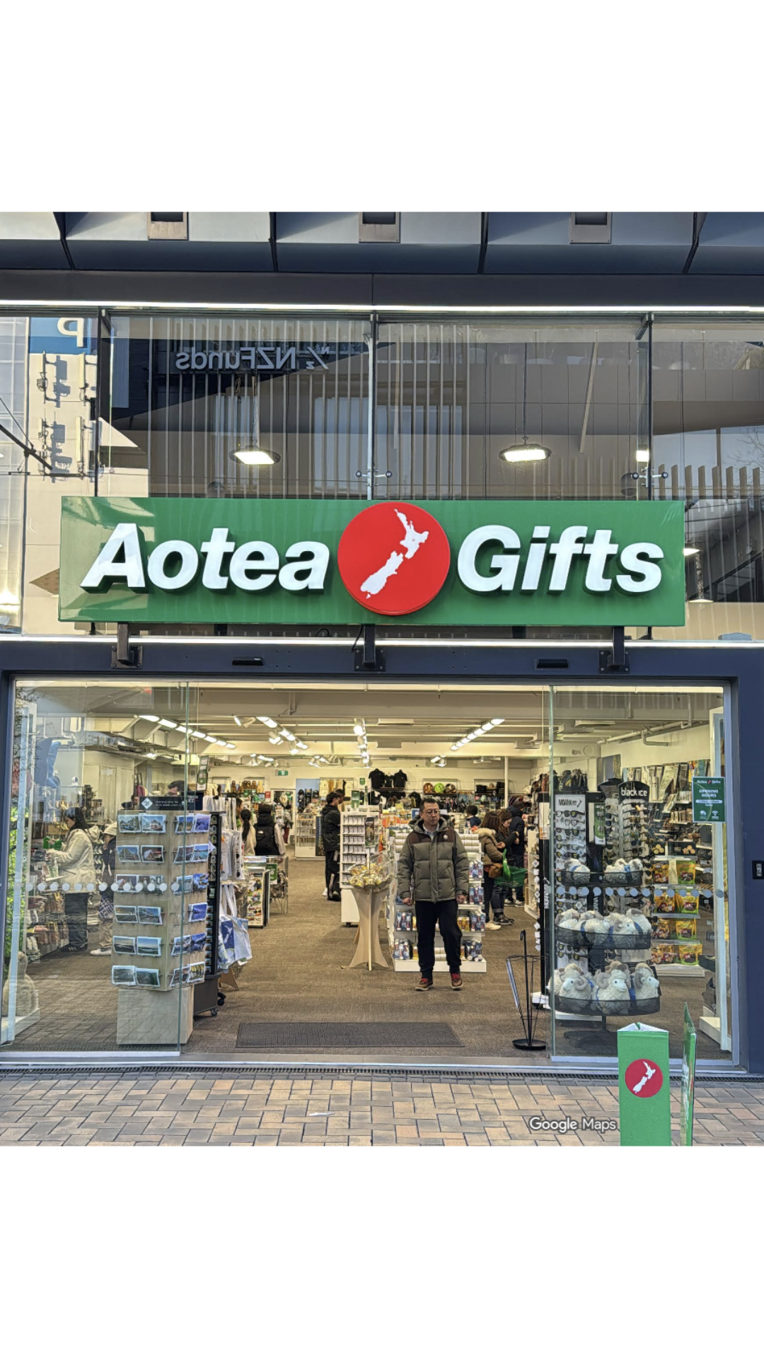 Exterior view of Aotea Gifts store with people shopping inside, sign with New Zealand map logo, and glass storefront.
