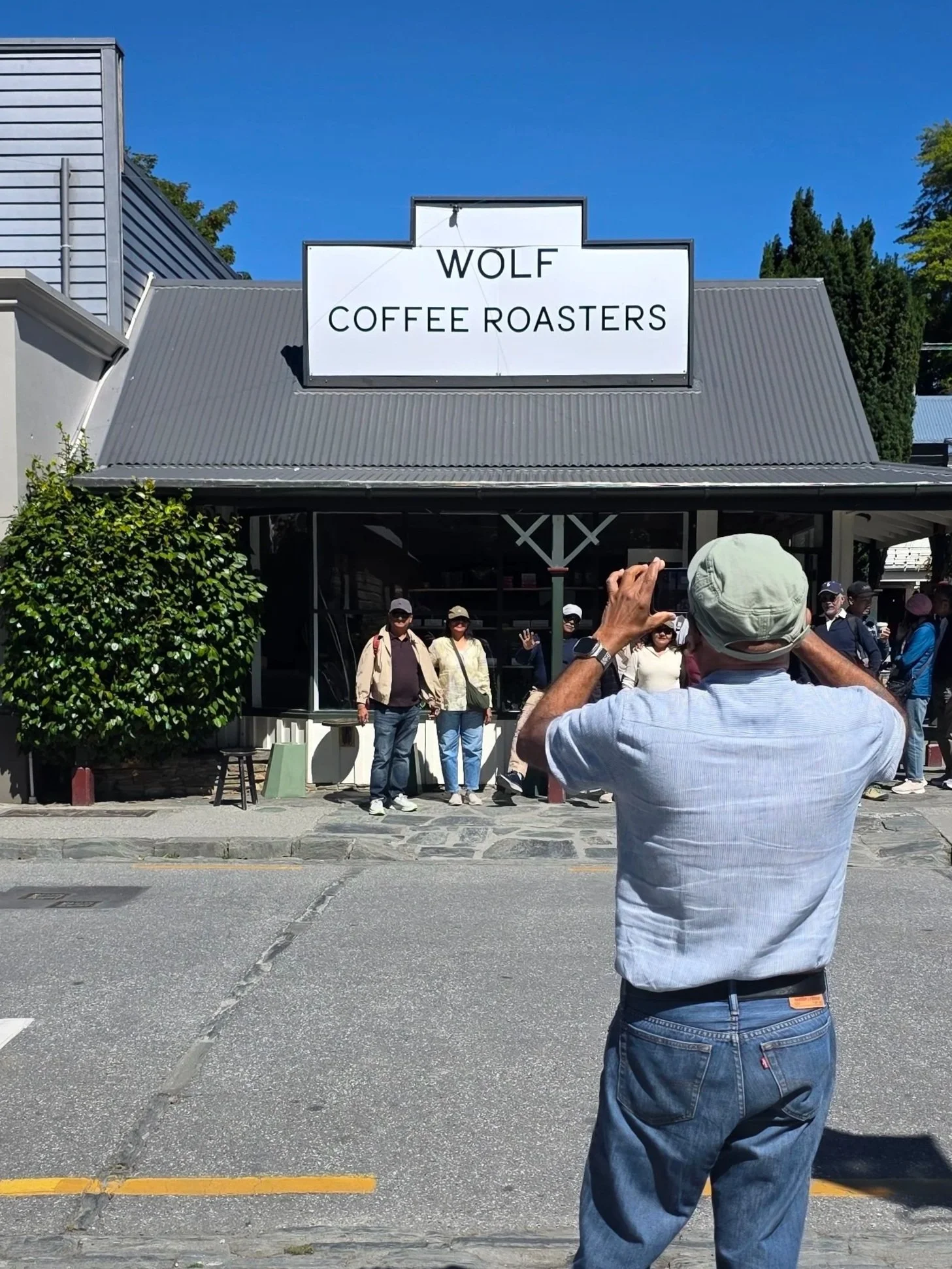 Front view of Wolf Coffee Roasters storefront with a group of people standing outside, and one person taking a photo of the scene.