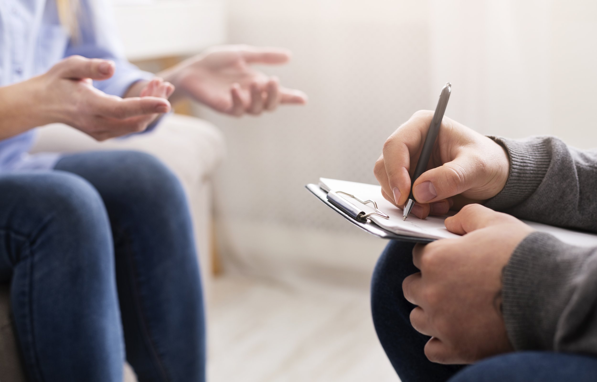 Close-up of a person in gray sweater writing on a clipboard held by another person, during a therapy or counseling session.