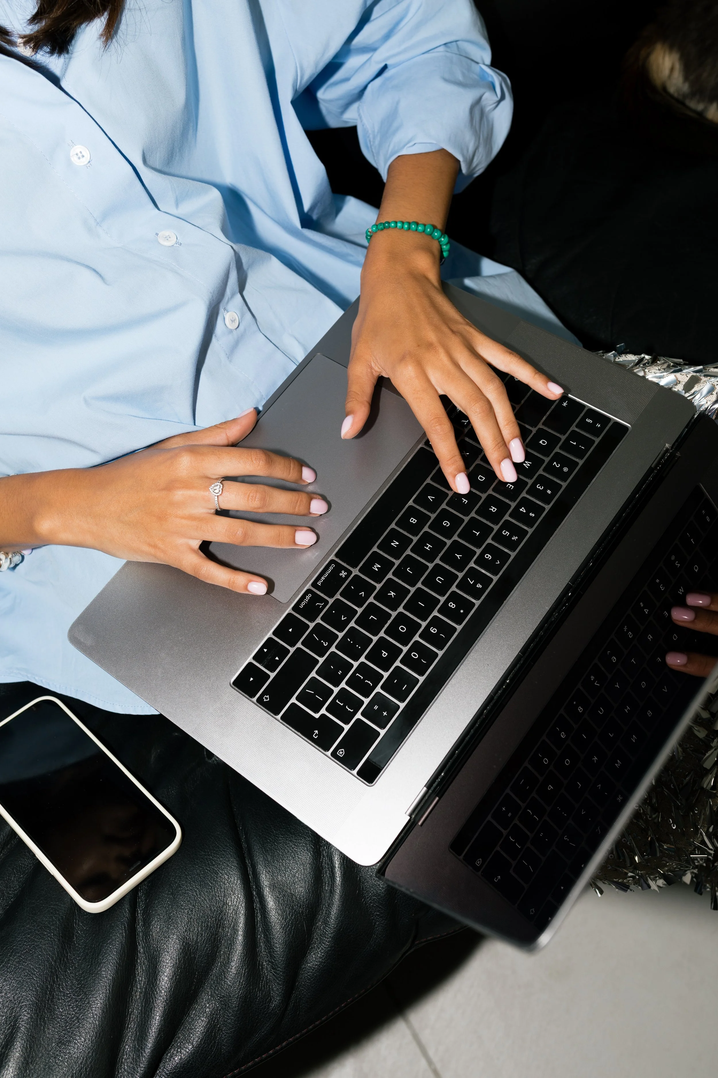 Person working on a laptop, seated on a black leather surface, with a smartphone nearby.