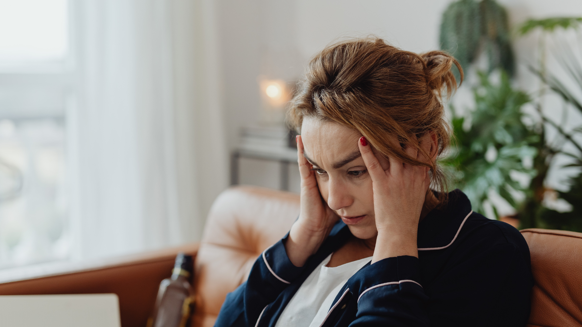 A woman sitting on a sofa holding her head with both hands, displaying a stressed or worried expression.