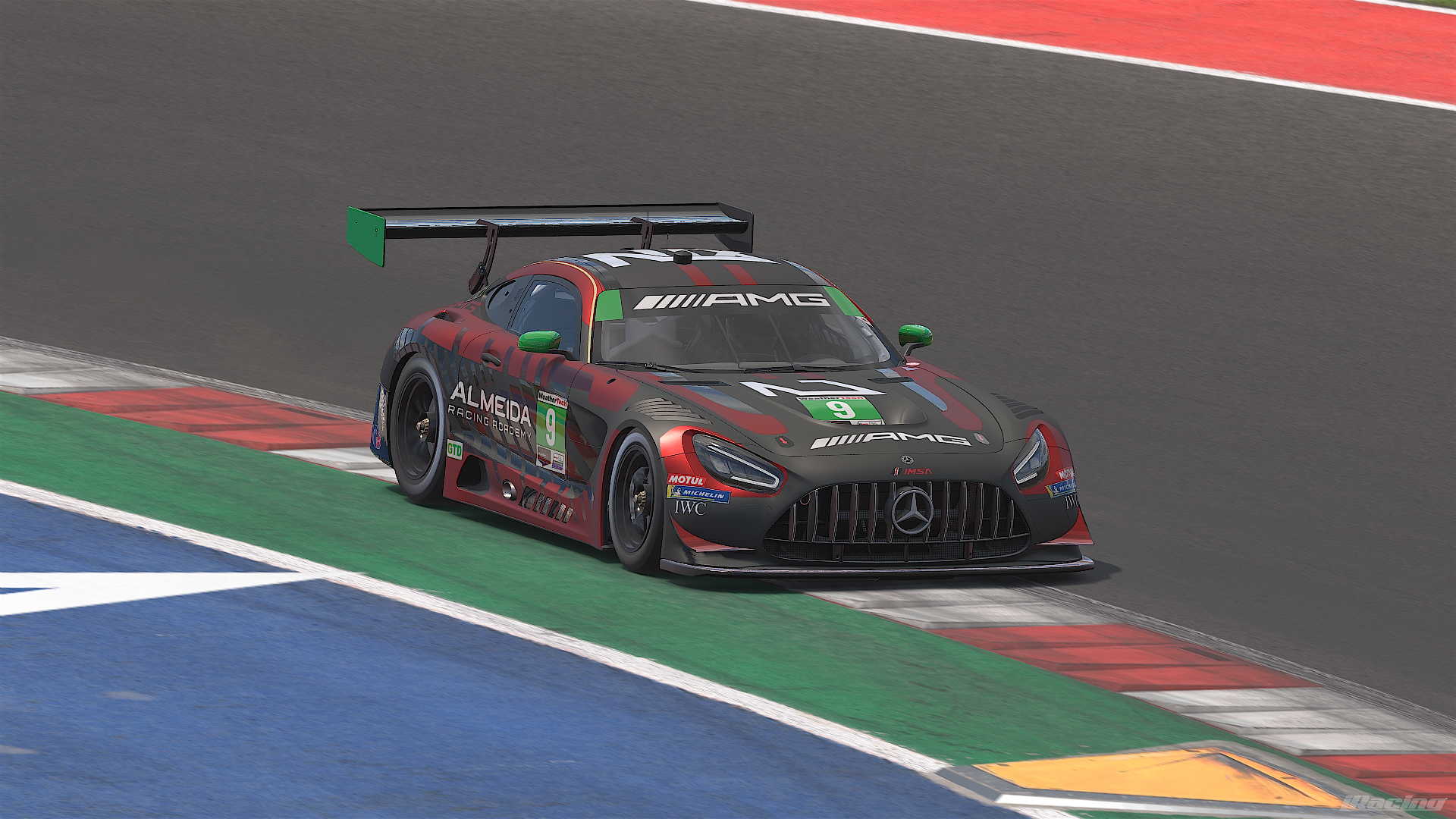 A Mercedes-AMG race car on a race track, positioned on the curb during a racing event. The car features a black and red paint scheme with sponsor logos, including AMG, Almeida Racing Academy, and others.