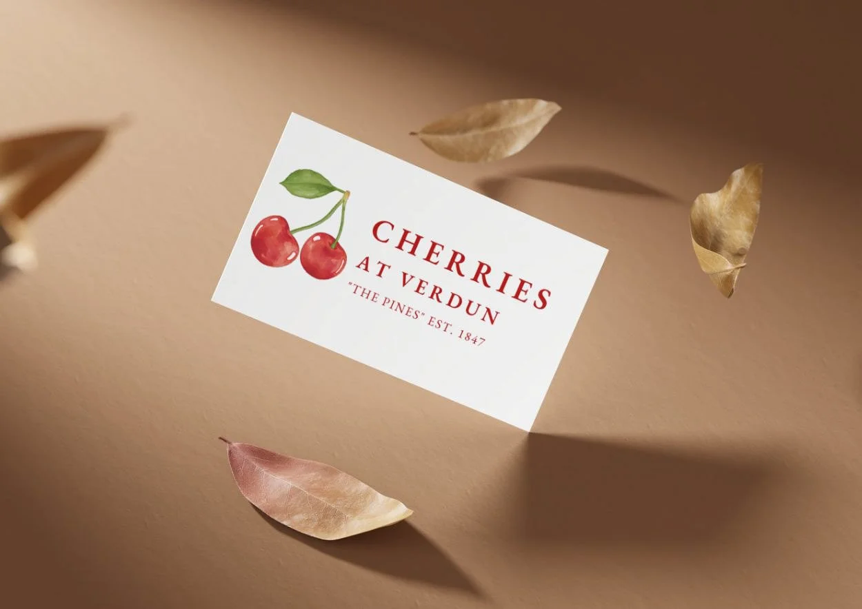 A business card for Cherries at Verdun with an illustration of two cherries and green leaves, surrounded by beige and brown dried leaves on a beige surface.