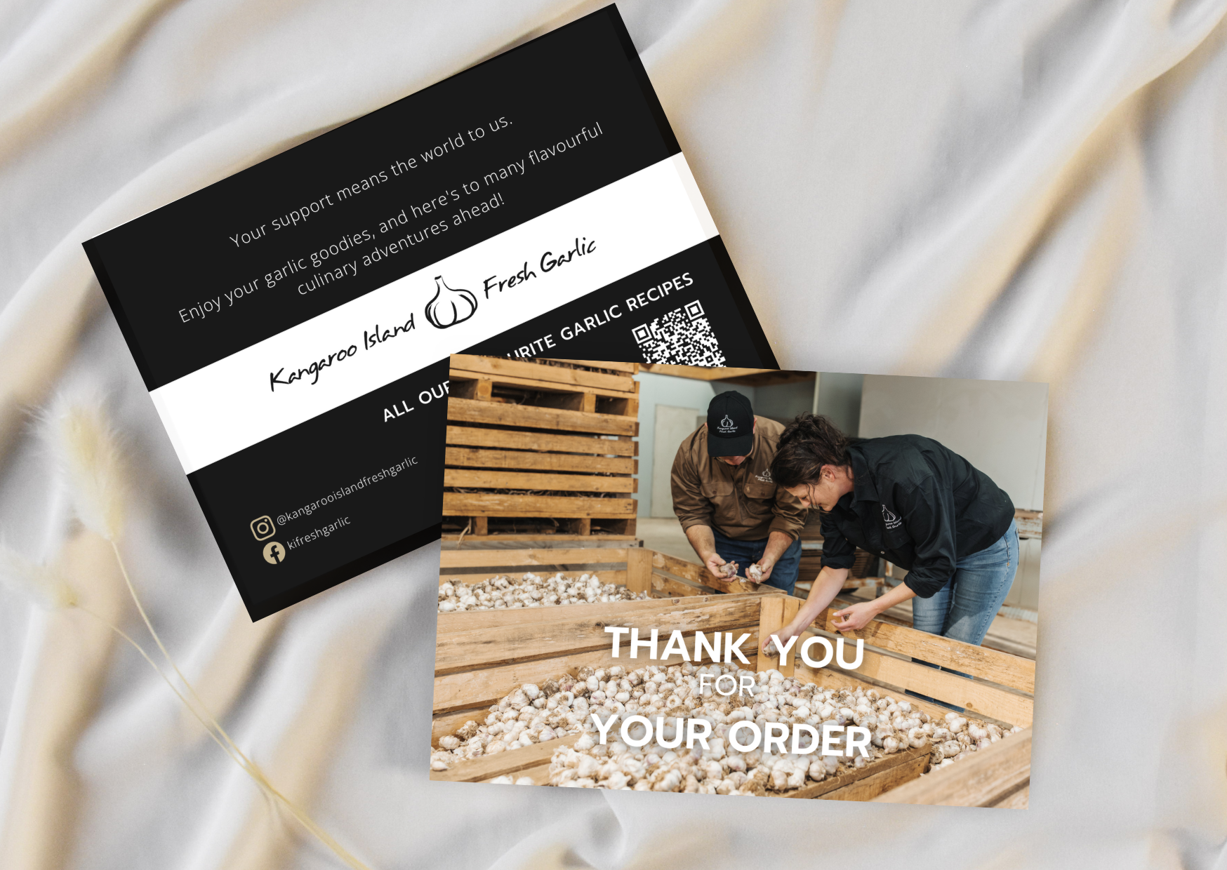 A thank you card from Kangaroo Island Fresh Garlic featuring a photograph of two people inspecting garlic in a wooden crate, placed on a silky, cream-colored fabric background.