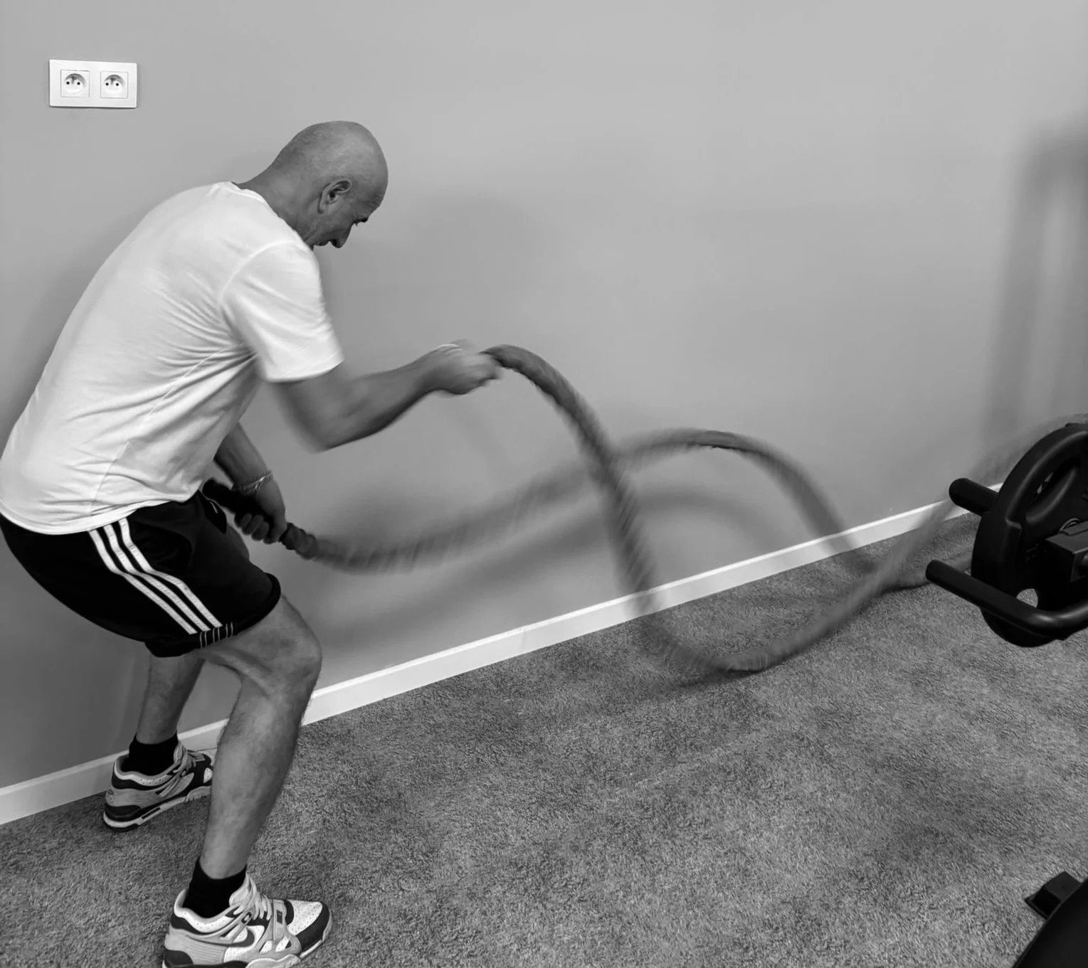 Un homme fait de l'exercice avec une corde à sauter dans une pièce, vue de profil.