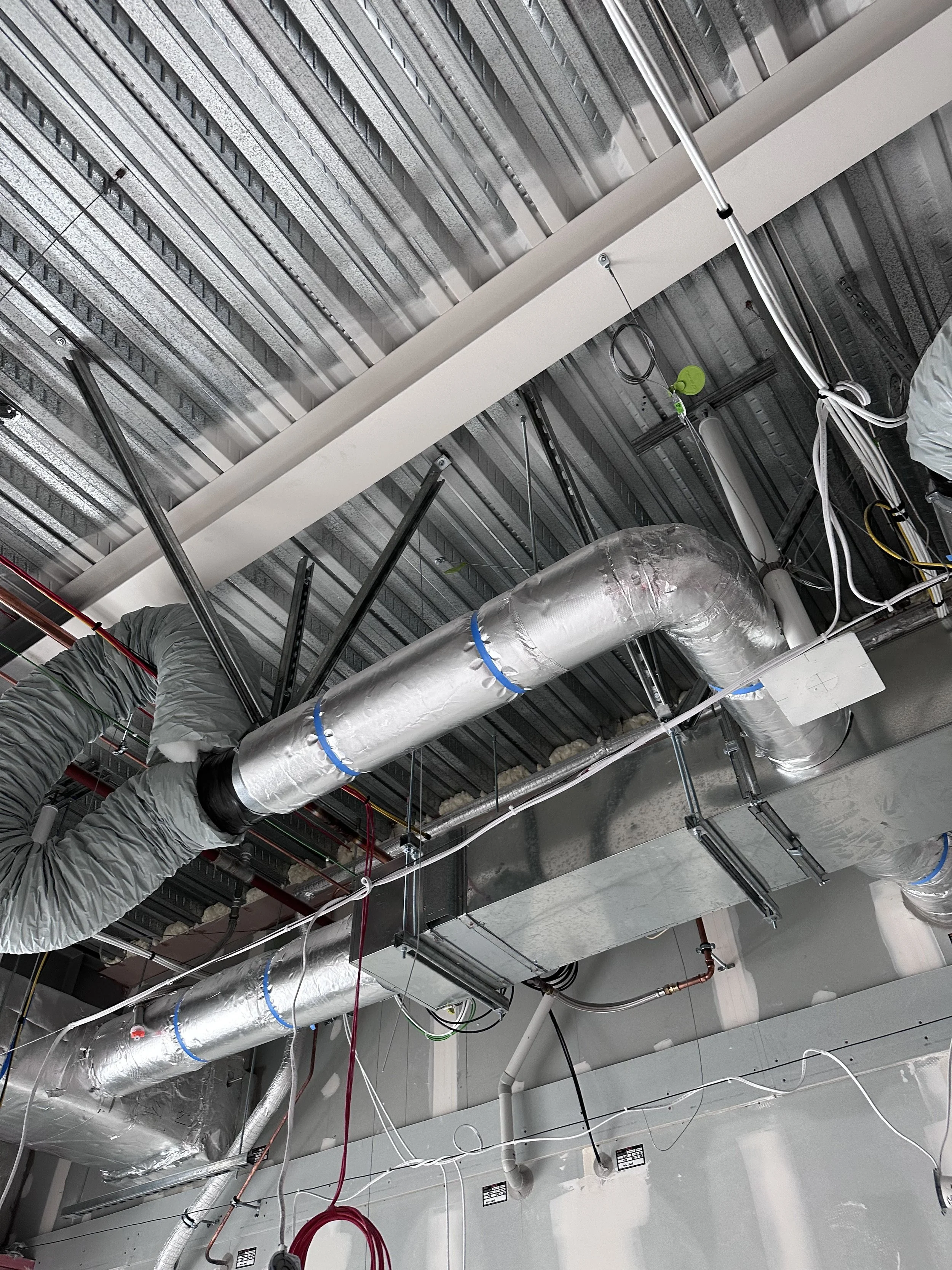 Ceiling with metallic HVAC ductwork, power cables, and electrical components in an industrial or commercial building.