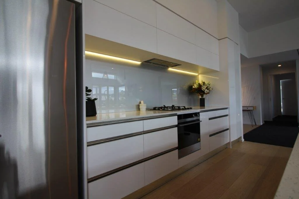 Modern kitchen with white cabinets, a black built-in oven, a gas stove, a vase with flowers, and a reflective backsplash.