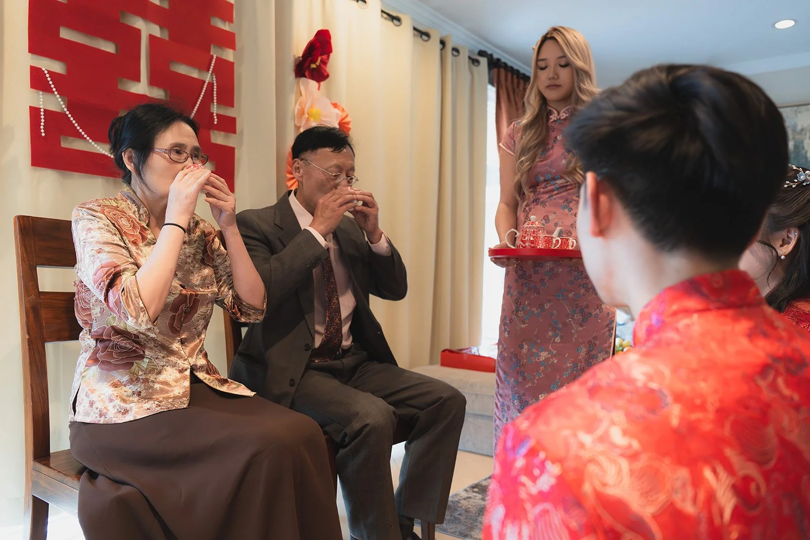 Family participating in a traditional tea ceremony during a Chinese wedding, with family members sitting and drinking tea, and an event host serving tea on a tray.