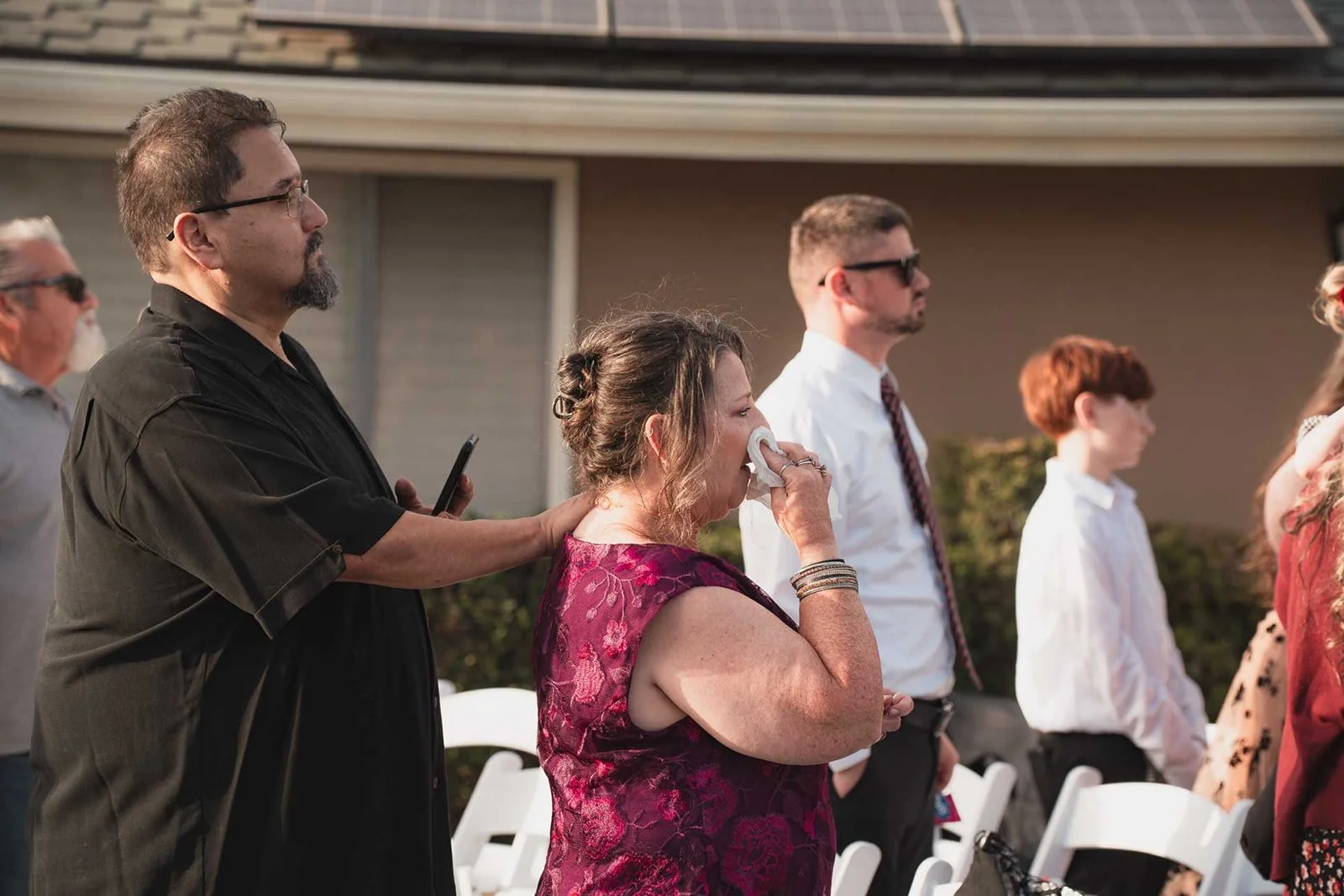 People attending an outdoor event, with some standing and one woman crying while holding a tissue.