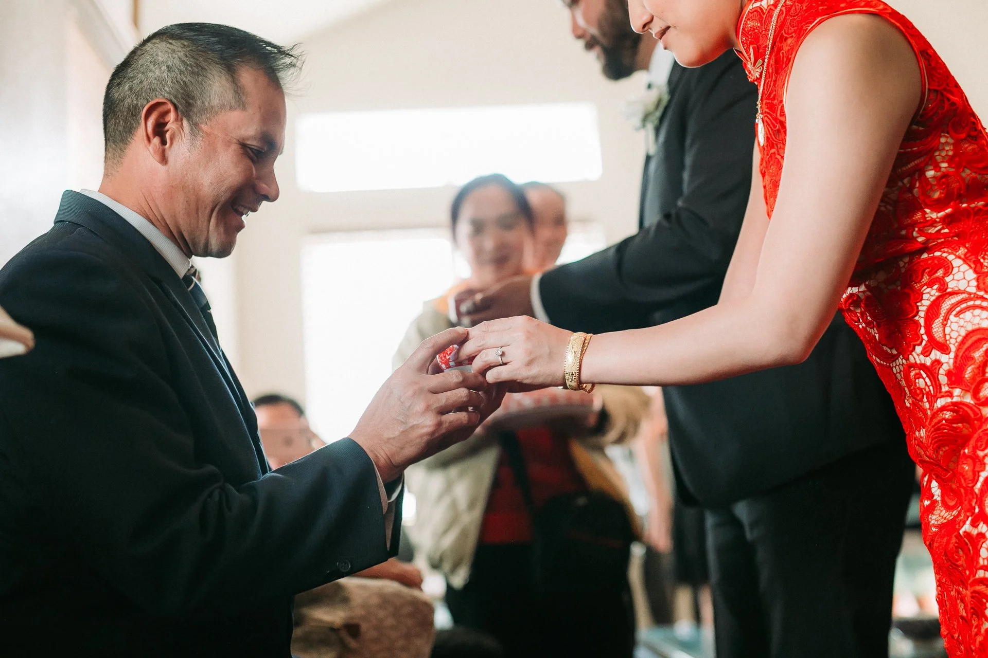 Man in a suit is proposing marriage to a woman in a red lace dress during a wedding ceremony.