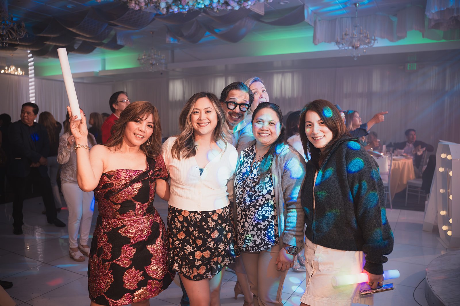 Group of five women smiling at a party, with colorful lighting and a dance floor in the background.