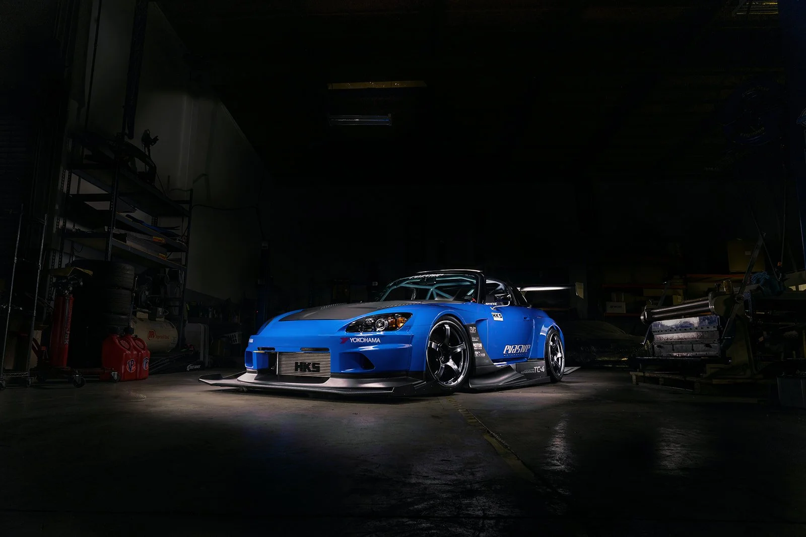 A blue racing car with wide wheels and aerodynamic features in a dimly lit garage or workshop.