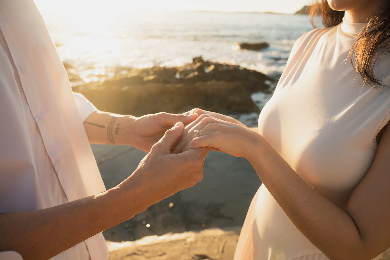 A man and woman exchanging rings at the beach during sunset.