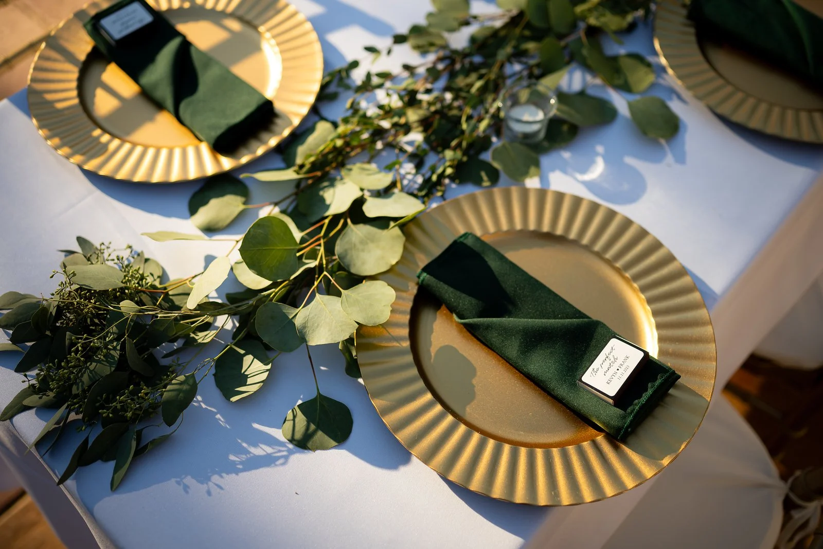 Table setting with gold plates, green napkins, and greenery centerpiece