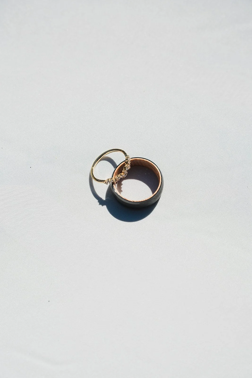 Close-up of two rings, one with small diamonds and the other a plain band, on a white surface with shadows.