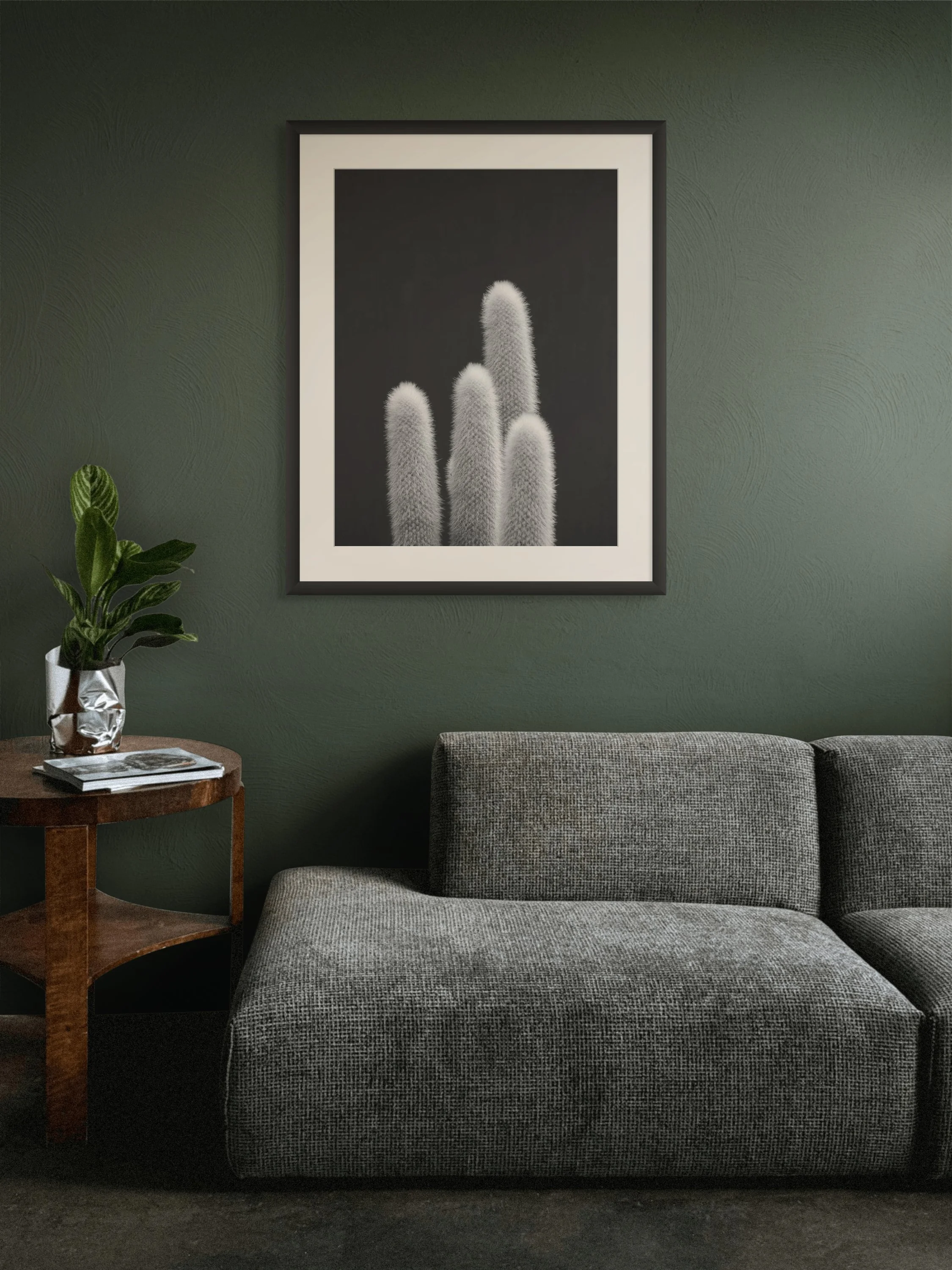Living room with green textured wall, framed black and white cactus photo, gray upholstered couch, and wooden side table with potted plant and magazines.