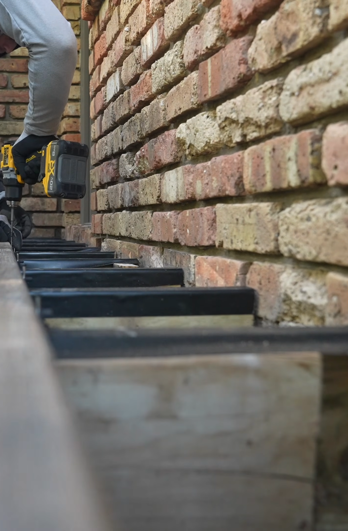 A person installing or repairing a piano keyboard against a brick wall, using a cordless drill with a yellow and black design.