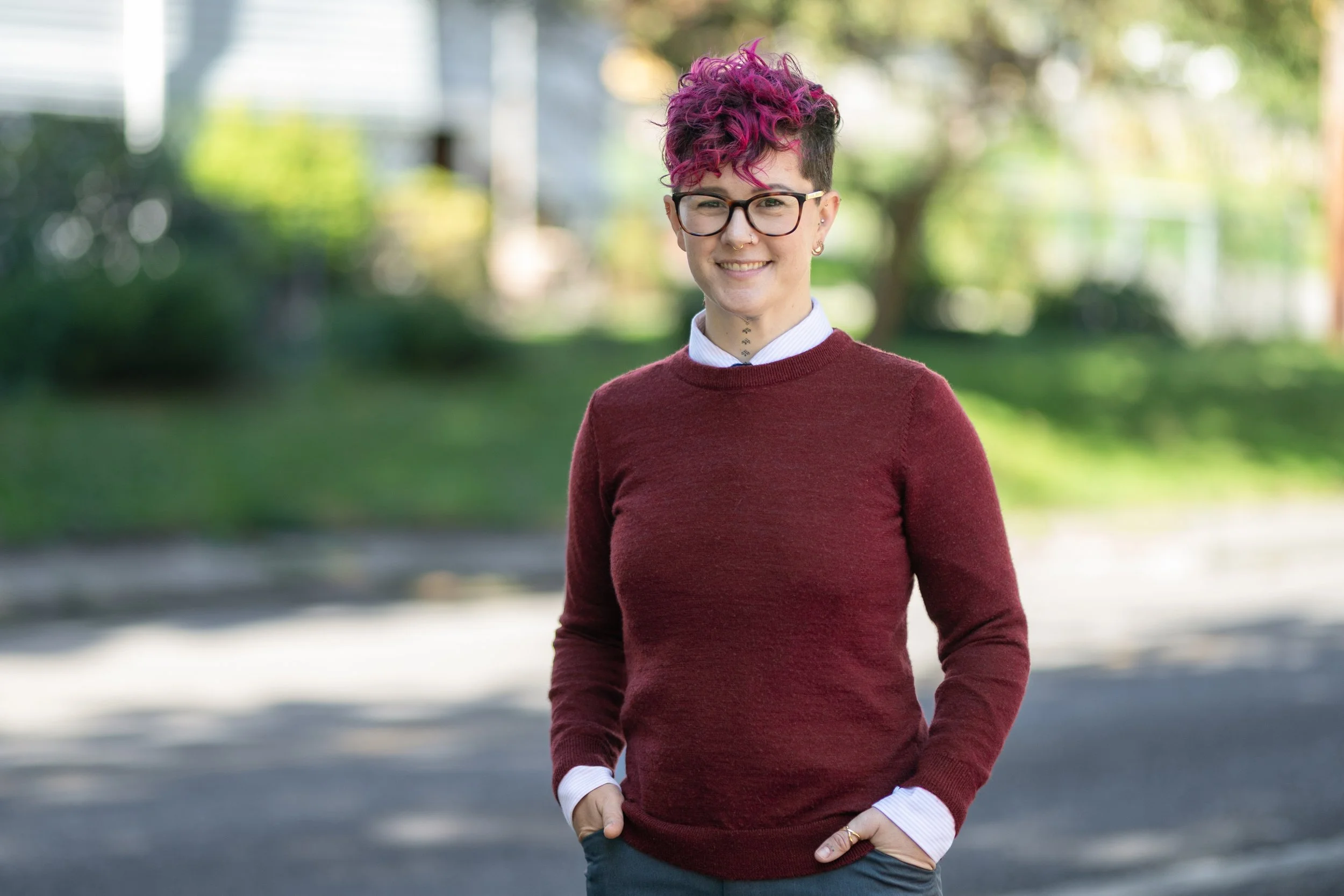 Queer woman with pink hair, glasses, and burgundy sweater on