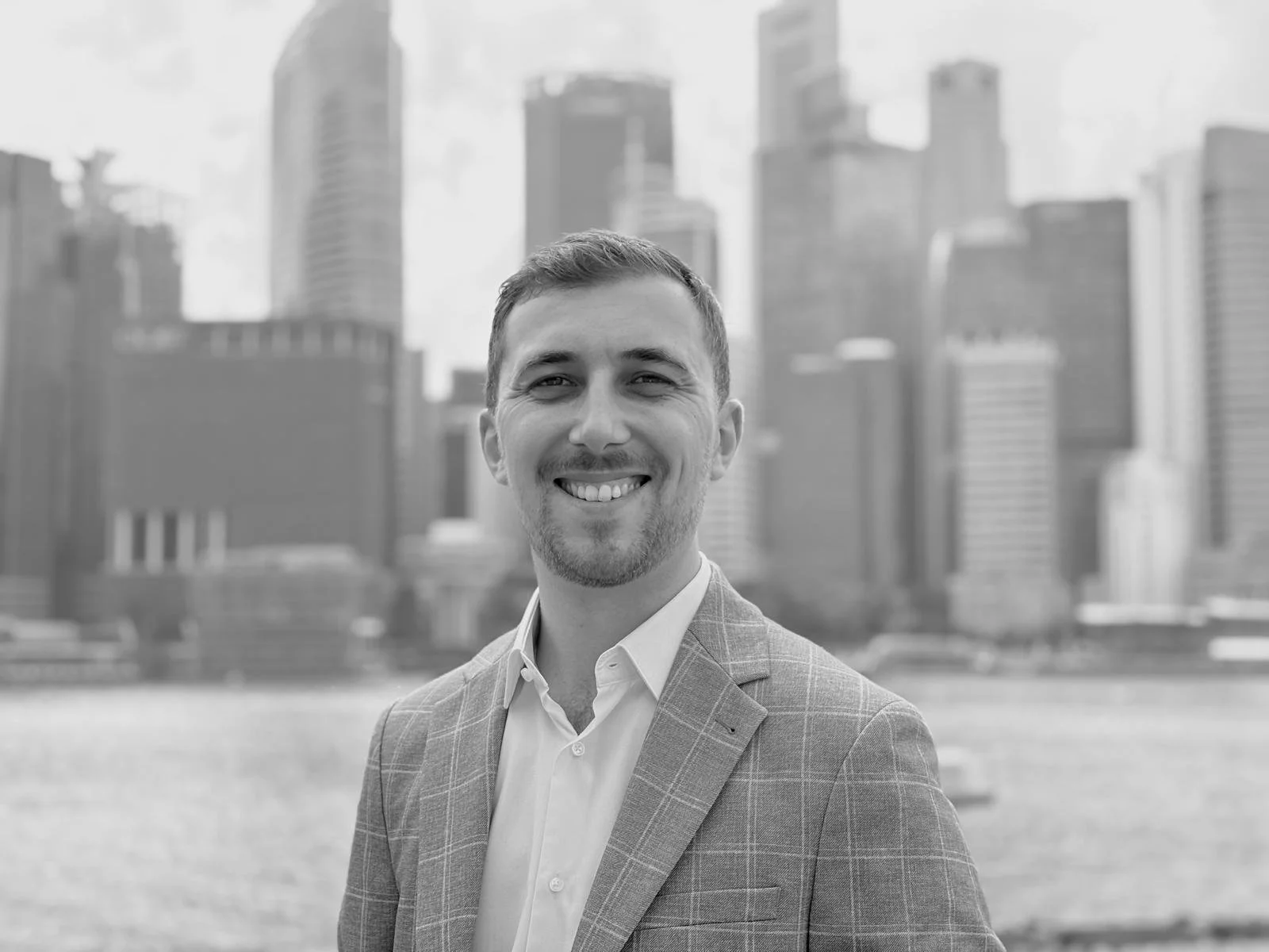 A smiling man wearing a suit jacket and white shirt with a city skyline in the background.