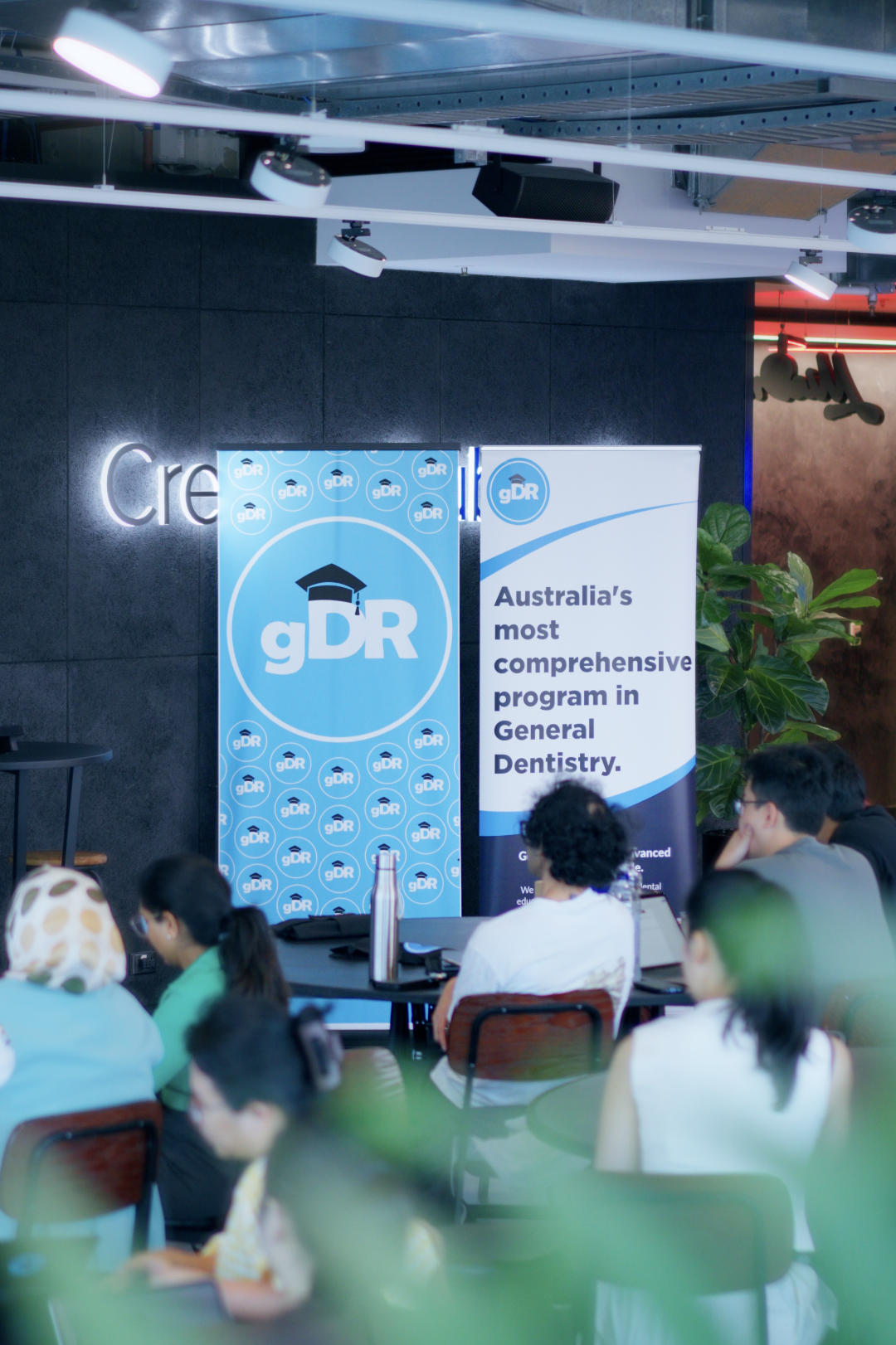 People attending a presentation at an event with banners that read 'gDR' and 'Australia's most comprehensive program in General Dentistry.'