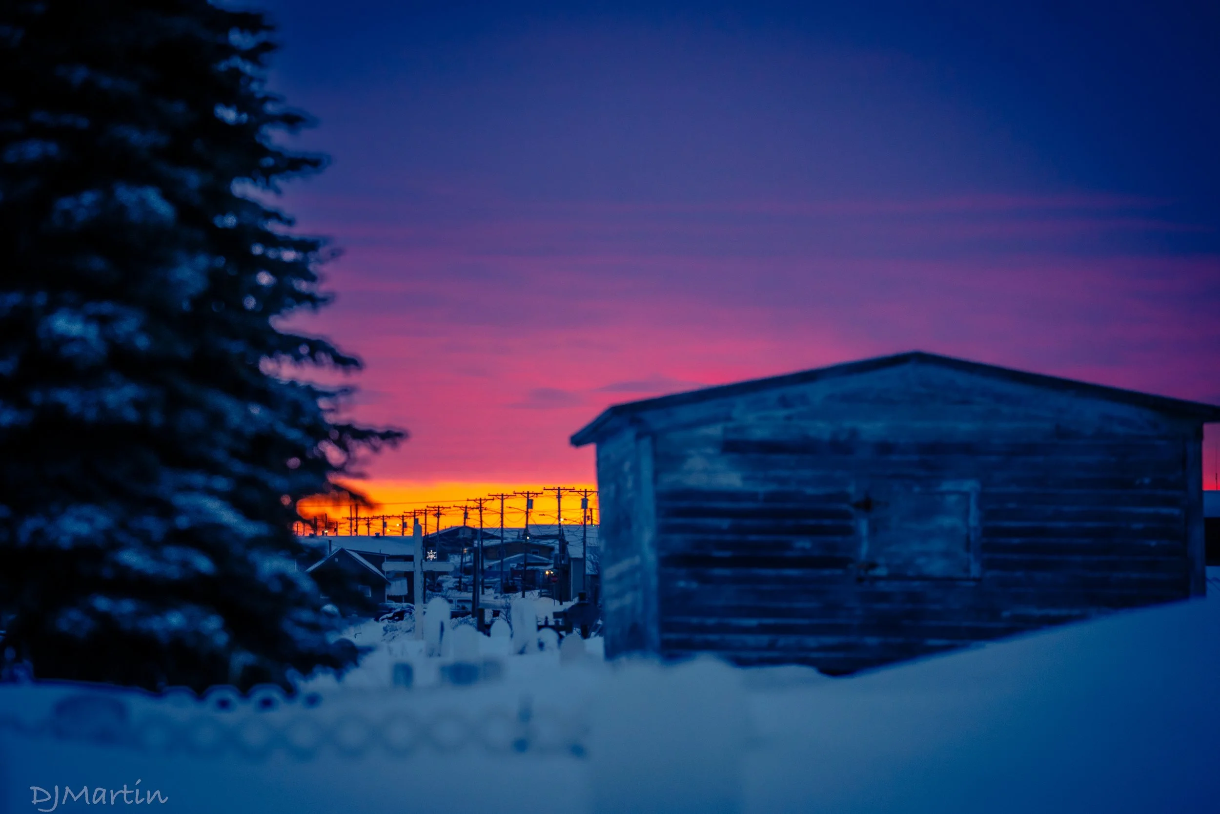 Fiery orange and purple sunrise over the historic Pioneer Cemetery in Nome, Alaska during winter.